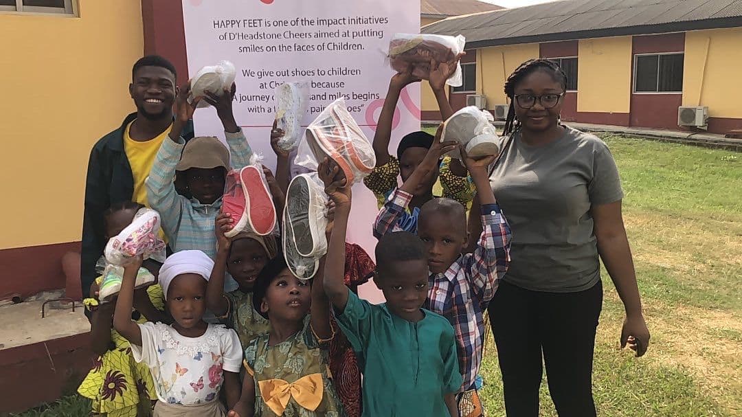 Children and volunteers holding shoes in front of a Happy Feet banner